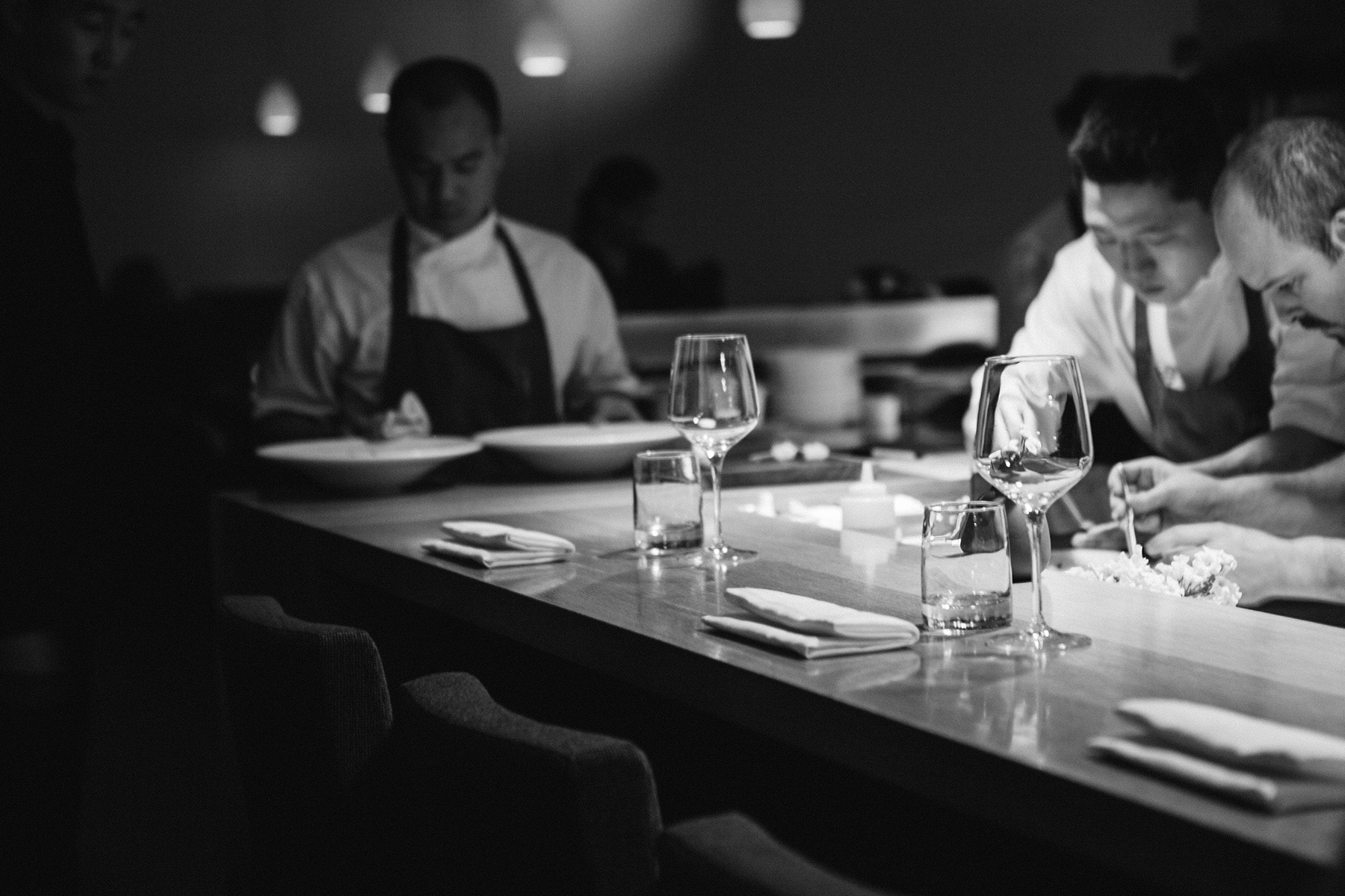Black-and-white view of chefs plating at the dining counter at Commis